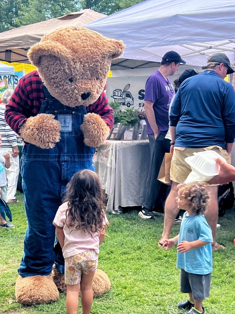 Two children meeting the Vermont Teddy Bear on the green